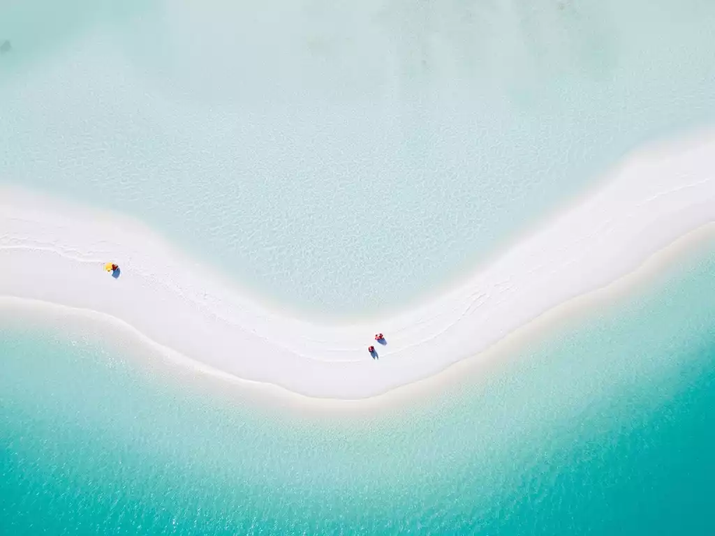 Aerial view of a pristine beach with turquoise water and white sand, typical of Sanibel Island, with a few people enjoying the sun and calm sea, no text, no words, no typography, clean image